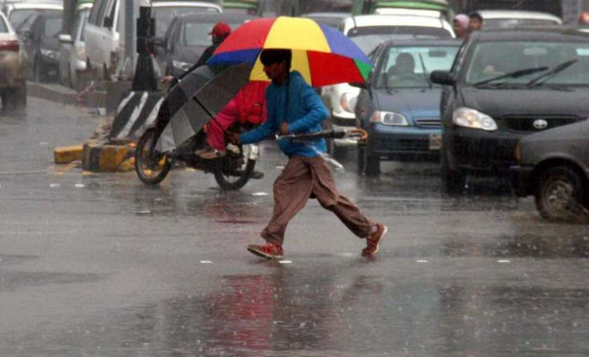 لاہور: شہر میں ہونے والی بارش کے دوران ایک نوجوان چھتری تانے ..