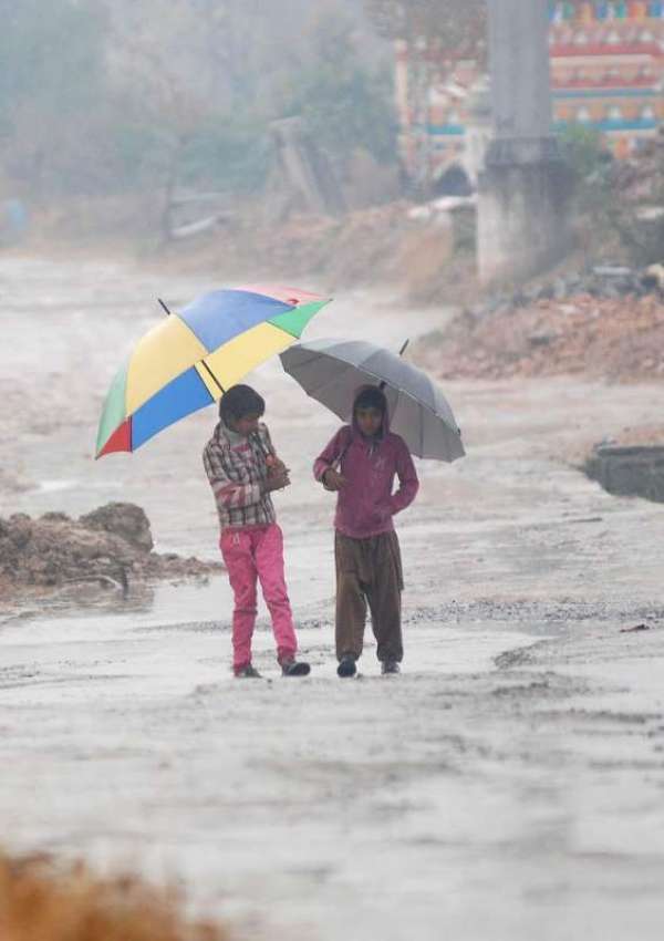 اسلام آباد: دو بچے بارش سے بچنے کے لیے چھتری تانے جا رہے ہیں۔