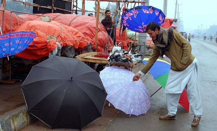 فیصل آباد: ایک محنت کش سڑک کنارے چھتریاں فروخت کے لیے سجائے ..
