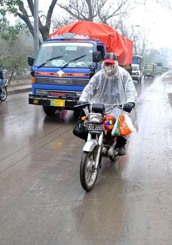 لاہور: ایک موٹر سائیکل سوار بارش سے بچنے کے لیے پلاسٹک اوڑھے ..