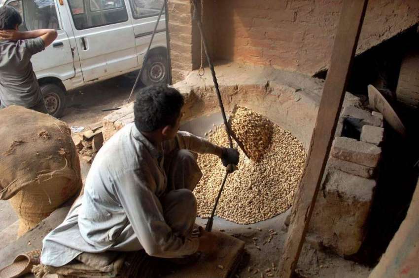 فیصل آباد: ایک محنت کش بھٹی میں مونگ پھلی بھون رہا ہے۔