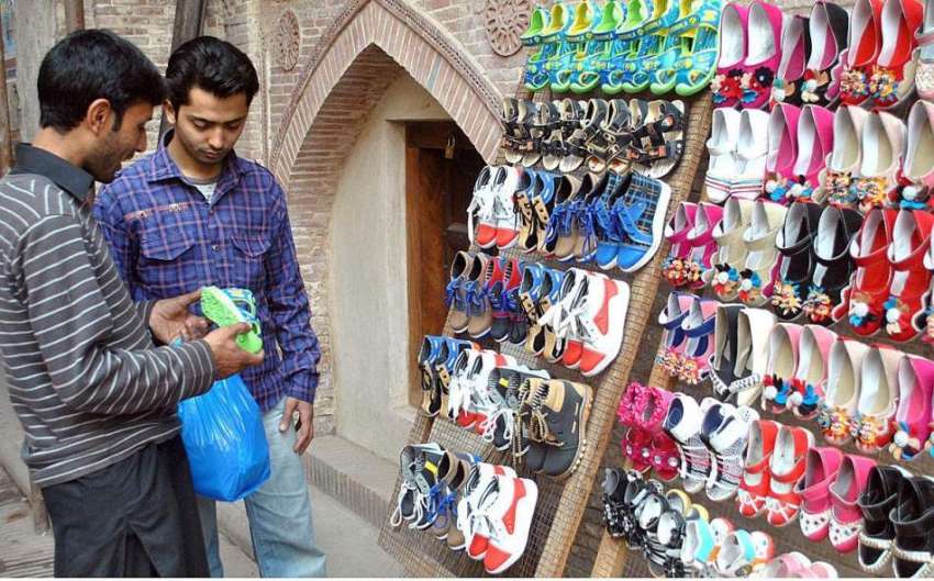 لاہور: ایک شہری سڑک کنارے لگے سٹال سے بچوں کے لیے جوتے پسند ..