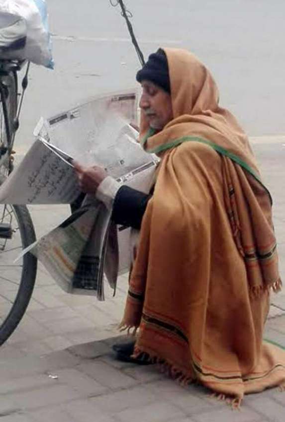 لاہور:ایک بزرگ شہری فٹ پاتھ پر بیٹھا اخبار پڑھ رہا ہے۔