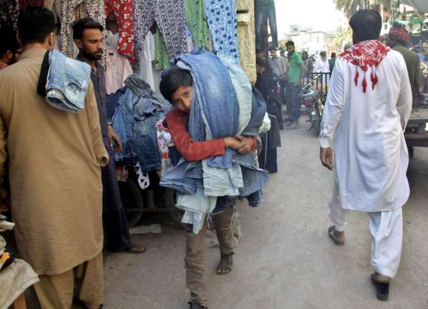لاہور: ایک بچہ لنڈا بازار میں پرانی پینٹیں کندھے پر رکھ کر ..