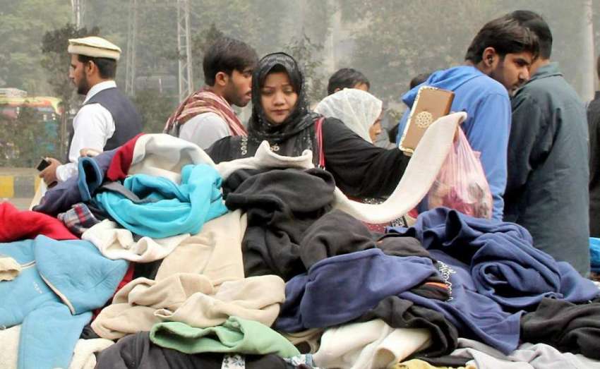 لاہور: ایک خاتون شادمان چوک میں ریڑھی سے گرم کپڑے خرید رہی ..