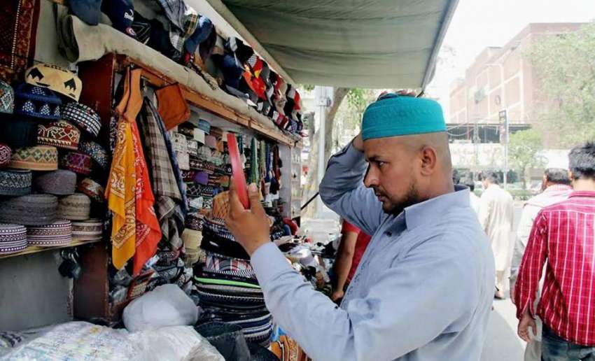 لاہور: مسجد شہداء کے باہر سٹال سے ایک شخص ٹوپی خریدنے کے ..
