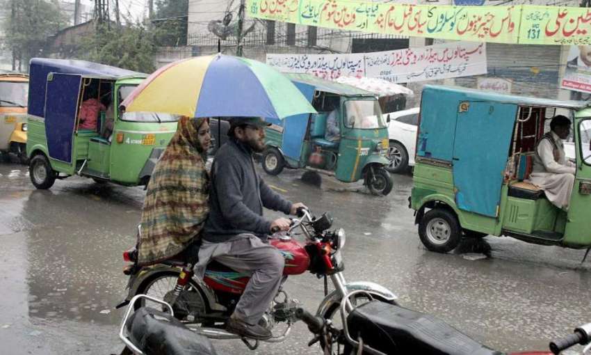 لاہور: موٹر سائیکل سوار فیملی بارش سے بچنے کے لیے چھتری تانے ..
