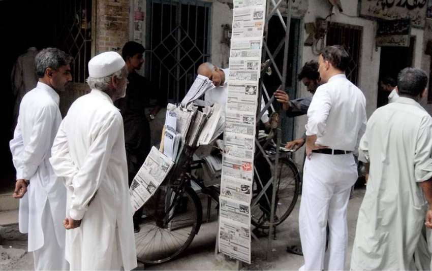 راولپنڈی: اخبار فروش نے اخبار سجا رکھے ہیں جبکہ شہری کھڑے ..