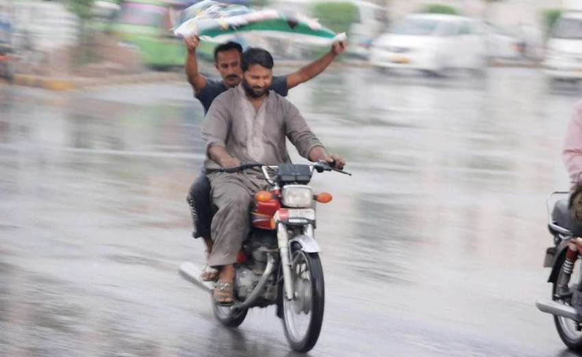 لاہور: موٹر سائیکل سوار بارش سے بچنے کے لیے اپنے سروں کو ..