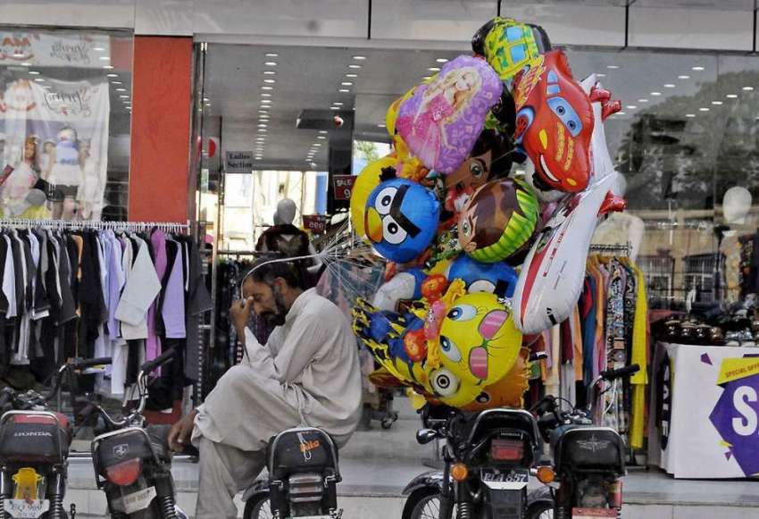 راولپنڈی: صدر بازار میں ایک محنت کش غبارے سجائے سائے میں ..