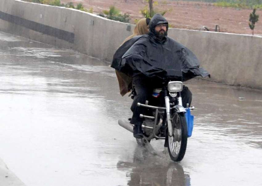 راولپنڈی: ایک موٹر سائیکل سوار بارش سے بچنے کے لیے برساتی ..