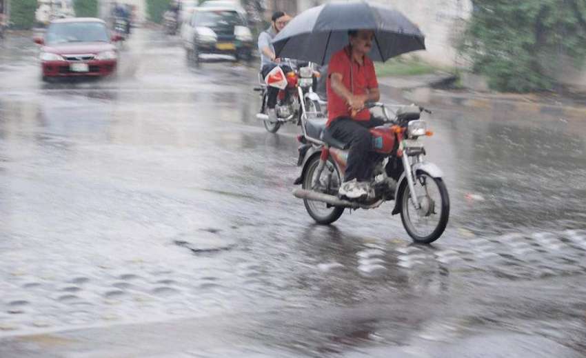 لاہور: موٹر سائیکل سوار بارش سے بچنے کے لیے چھتری تانے جار ..