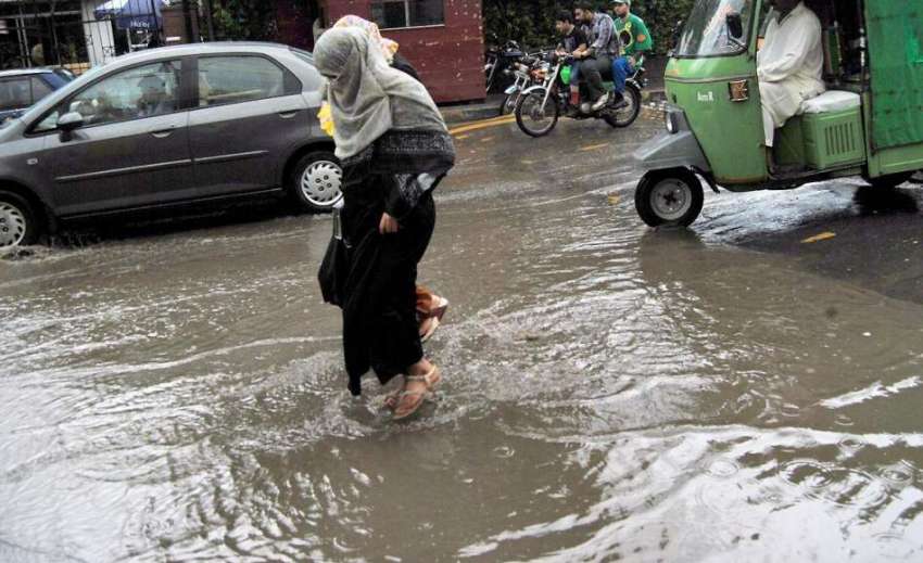 لاہور: شہر میں ہونیوالی بارش کے بعد سڑک پر کھڑے پانی سے خواتین ..