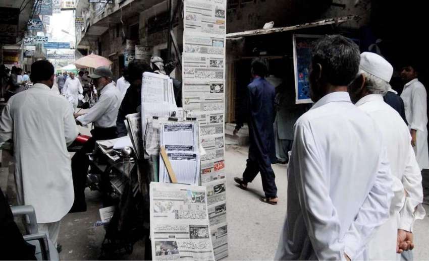 راولپنڈی: اخبار فروش نے اخبار سجا رکھے ہیں جبکہ شہری کھڑے ..