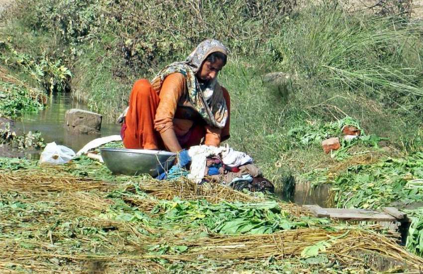 فیصل آباد: ایک خاتون نہری پانی سے کپڑے دھو رہی ہے۔