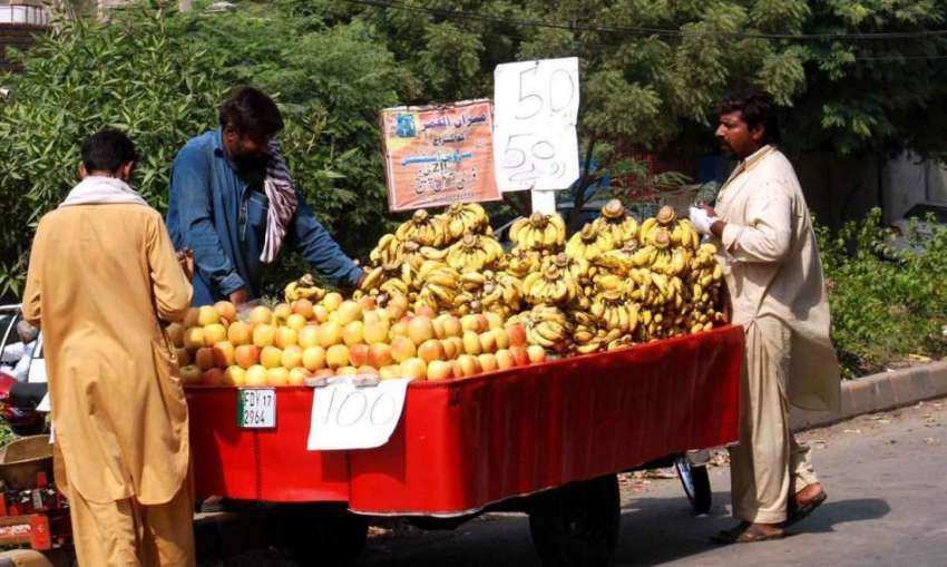 فیصل آباد: محنت کش چنگچی پر فروخت کے لیے فروٹ سجا رہا ہے۔