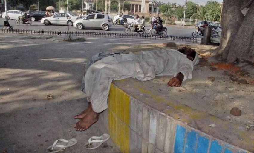 لاہور: ایک بھکاری دوپہر کے وقت چیئرنگ کراس چوک میں درخت کے ..