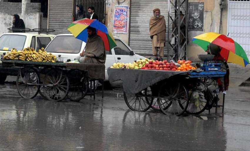 راولپنڈی: پھل فروش بارش سے بچنے کے لیے چھتری تانے گاہکوں ..