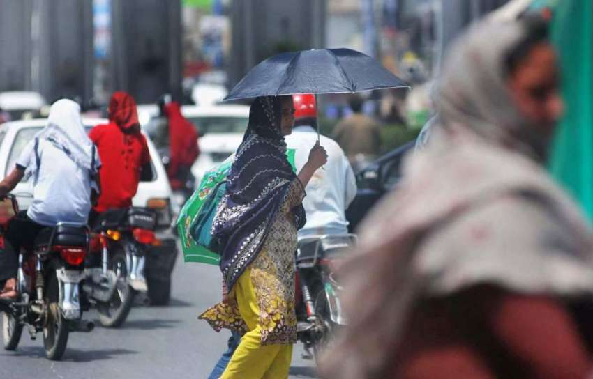 ایک خاتون دھوپ کی شدت سے بچنے کیلئے چھتری تانے جا رہی ہے