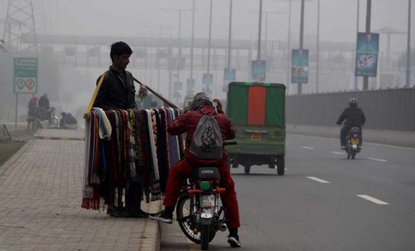 لاہور: موٹر سائیکل سوار شہری سردی کی شدت سے بچنے کے لیے سڑک ..