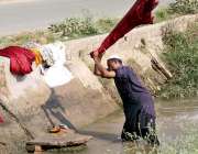 سرگودھا: ایک شخص نہر کے اندر کھڑا ہو کر کپڑے دھو رہا ہے۔