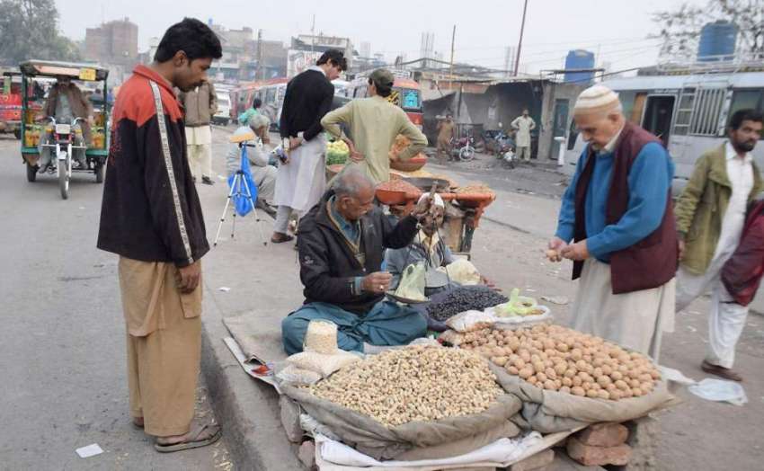 لاہور: ایک شہری فٹ پاتھ پر سجی دکان سے اخروٹ خرید رہا ہے۔