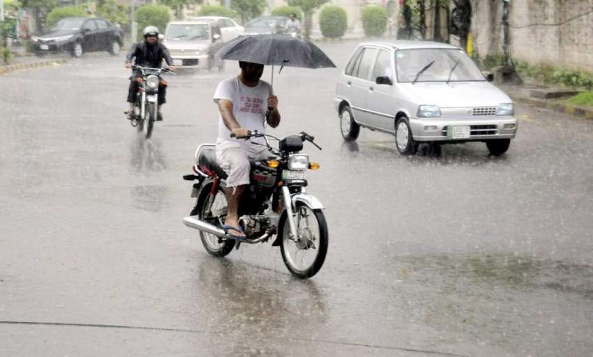 لاہور: شہر میں ہونیوالی بارش کے دوران ایک موٹر سائیکل سوار ..