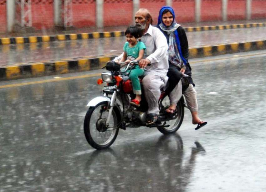لاہور: شہر میں ہونیوالی بارش کے دوران موٹر سائیکل سوار فیملی ..