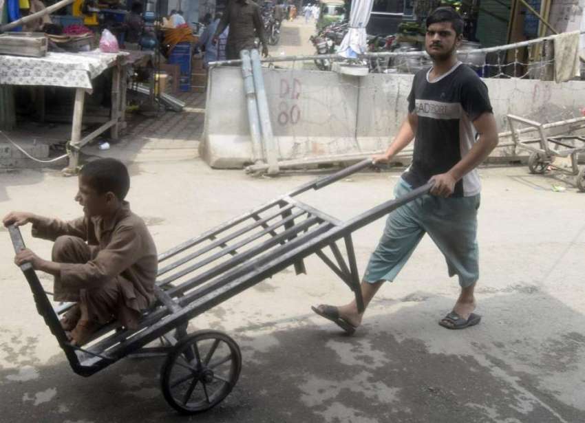 لاہور: ایک محنت کش ہتھ ریڑھی پر بچے کو بٹھا کر لیجا رہے ہیں۔