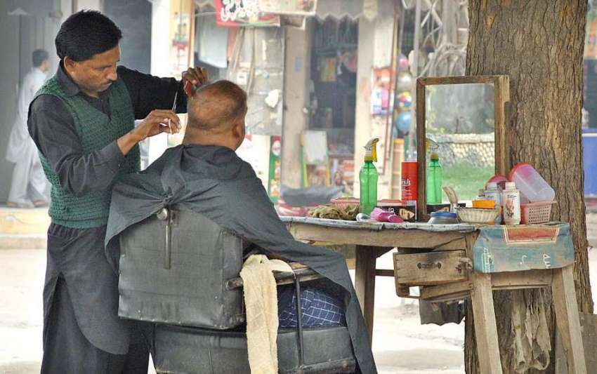 ملتان: انصاری چوک کے قریب ایک نائی گاہک کے بال کاٹ رہا ہے۔