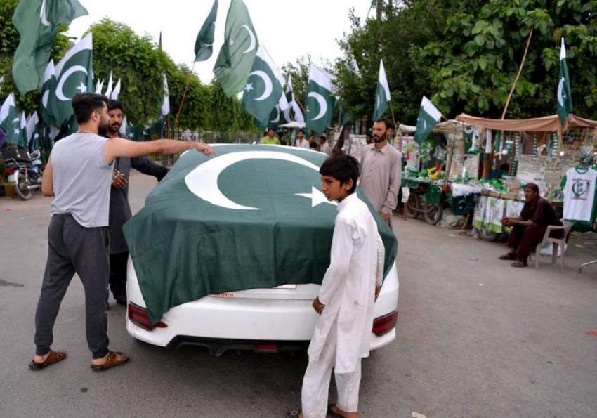 لاہور: جشن یوم آزادی کی آمد کے موقع پر دکاندار ایک کار کے ..