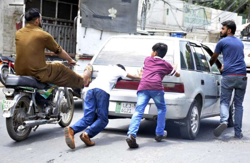 لاہور: بچے اور موٹر سائیکل سوار خراب گاڑی کو دھکا لگا رہے ..