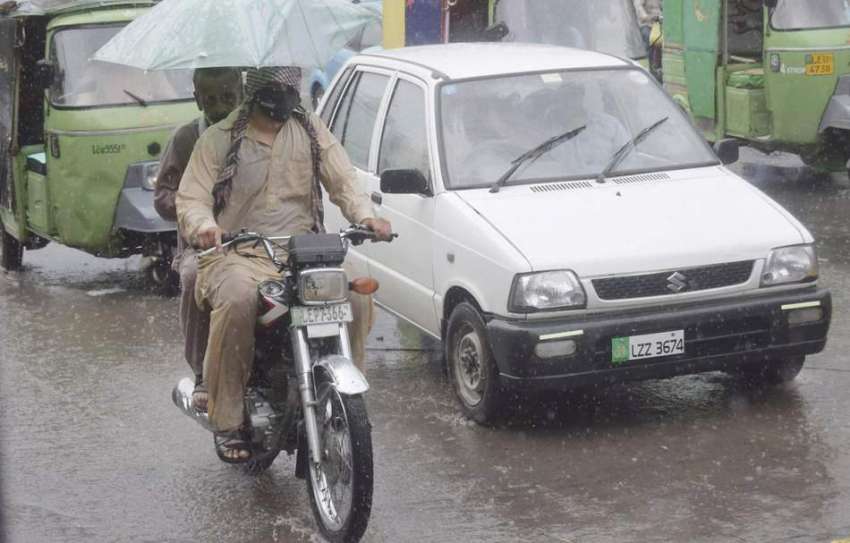لاہور: شہر میں ہونیوالی بارش کے دوران موٹر سائیکل سوار چھتری ..