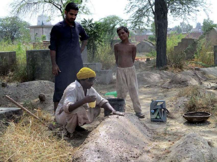 فیصل آباد: ایک شخص قبر پر مٹی کا لیپ کر رہا ہے۔