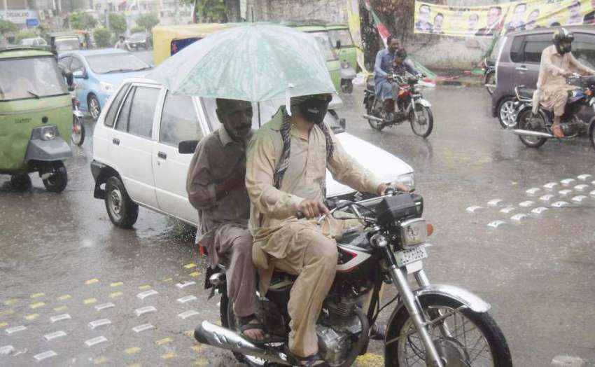 لاہور: شہر میں ہونیوالی بارش کے دوران موٹر سائیکل سوار چھتری ..