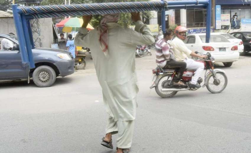 لاہور: ایک شخص اپنے سر پر چارپائیاں اٹھا کر لیجا رہا ہے۔
