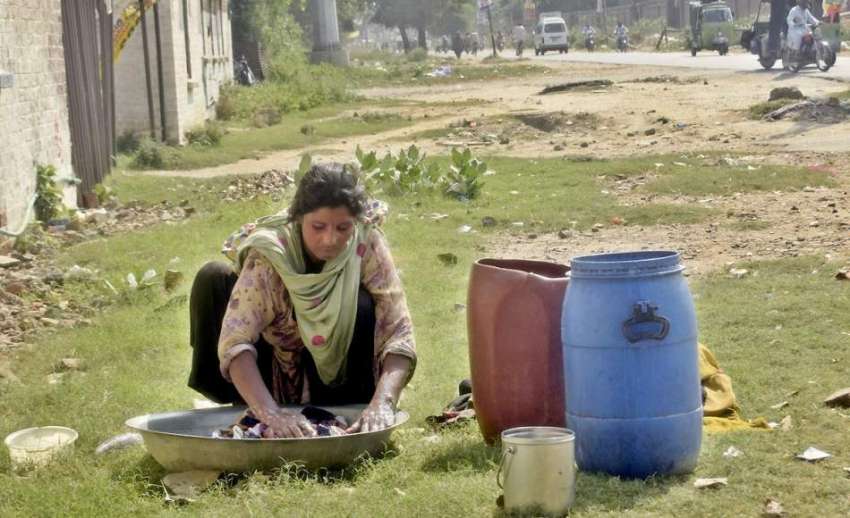 لاہور: خانہ بدوش خاتون سڑک کنارے بیٹھی کپڑے دھو رہی ہے۔