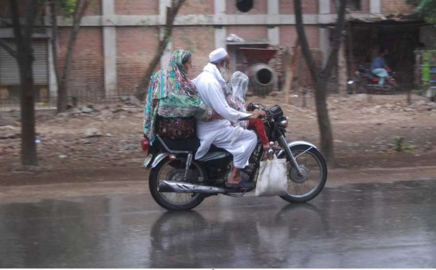 لاہور: شہر میں ہونیوالی بارش کے دوران موٹر سائیکل سوار فیملی ..
