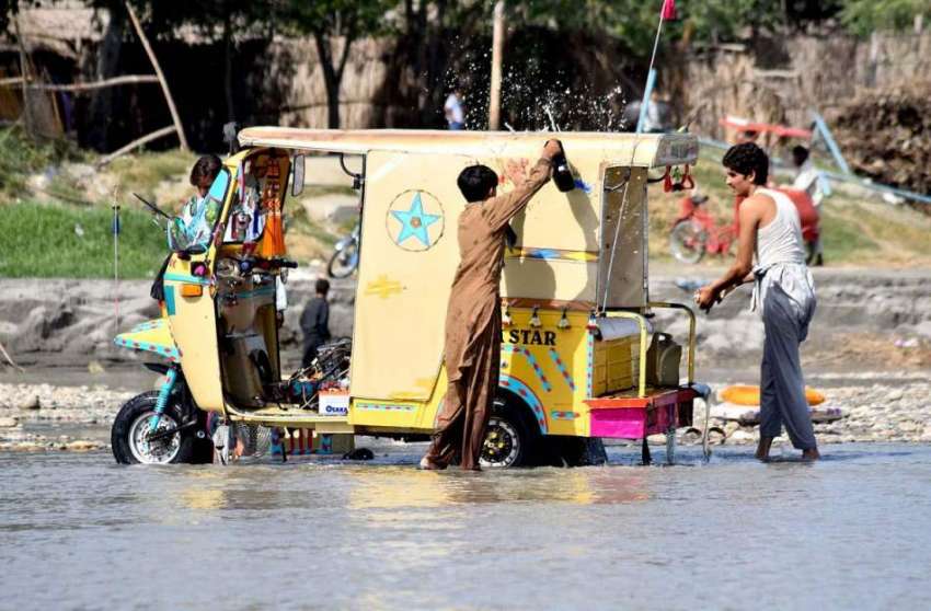پشاور: دو شخص سردایاب دریا کنارے رکشہ دھو رہے ہیں۔
