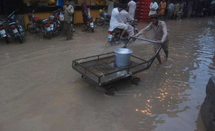 لاہور:محنت کش موسلا دھار بارش کے بعد سڑک پر جمع پانی میں ..