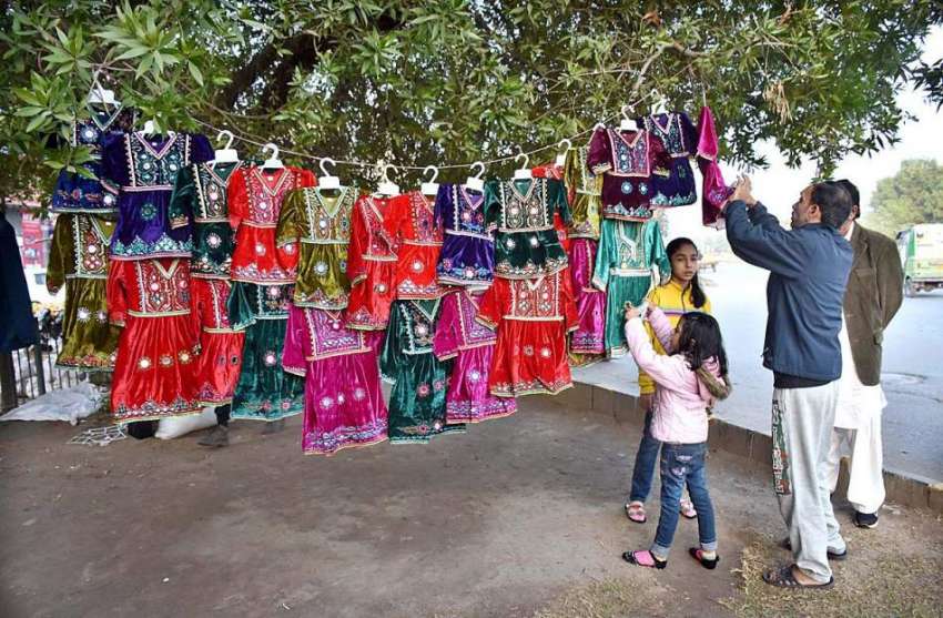 لاہور: سڑک کے بچوں کے روایتی رنگین لباس فروخت کرتے ہوئے ایک ..