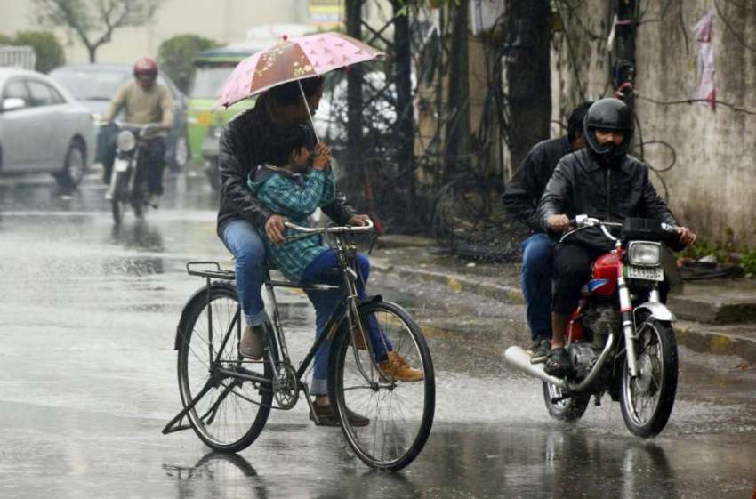لاہور: سائیکل سوار بارش سے بچنے کے لیے چھتری تانے جارہے ہیں۔
