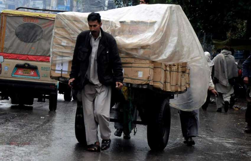راولپنڈی: بارش کے دران ایک مزدور نے اپنی ریڑھی کو پلاسٹک ..