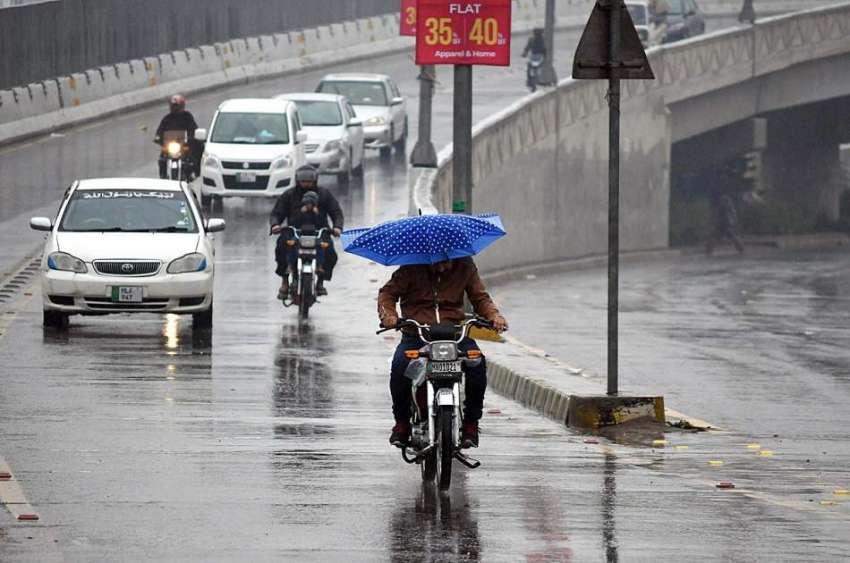 ملتان: بارش سے بچانے کے لئے ایک موٹرسائیکل سوار چھتری کی ..