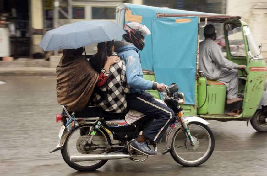 لاہور: موٹر سائیکل سوار فیملی بارش سے بچنے کے لیے چھتری تانے ..