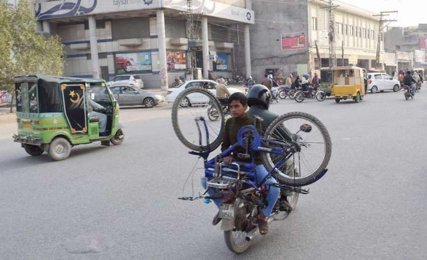لاہور: ایک موٹر سائیکل سوار شہری اپنے بیٹے کے لیے سائیکل ..