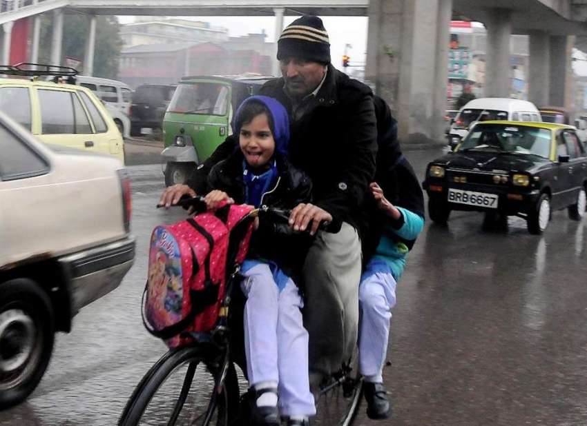 راولپنڈی: دوران بارش ایک شخص سائیکل پر اپنے بچوں کو سکول ..