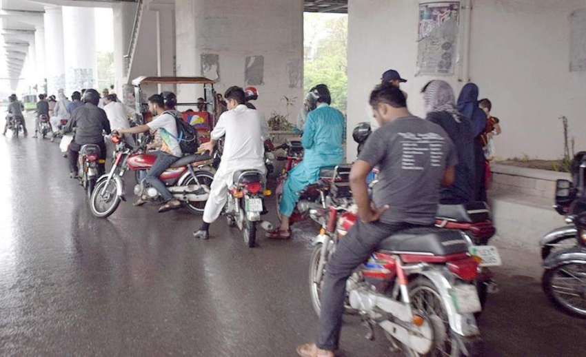 لاہور: موٹر سائیکل سوار شہری بارش سے بچنے کے لیے اورنج لائن ..