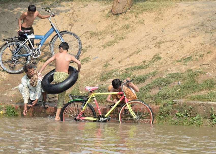 لاہور: نوجوان نہر میں نہانے کے بعد اپنی سائیکلیں دھو رہے ..