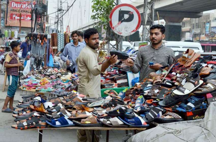 لاہور: ایک دکاندار اپنے سڑک کے کنارے اسٹال پر صارفین کو جوتیاں ..
